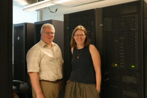 two professors smiling in front of larger computer servers