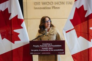 Woman speaking at a podium flanked by two flags of Canada